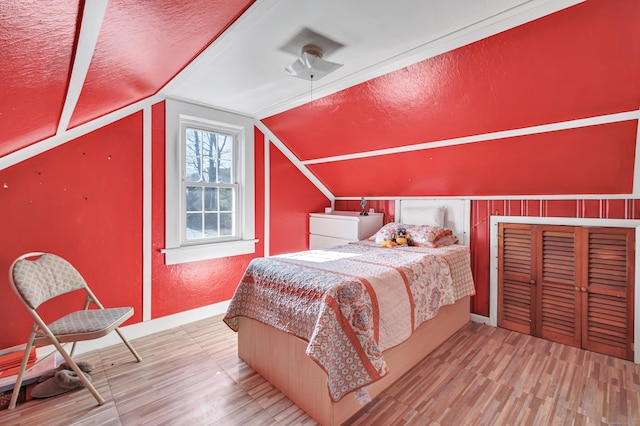 bedroom with a textured ceiling, wood finished floors, a textured wall, and vaulted ceiling