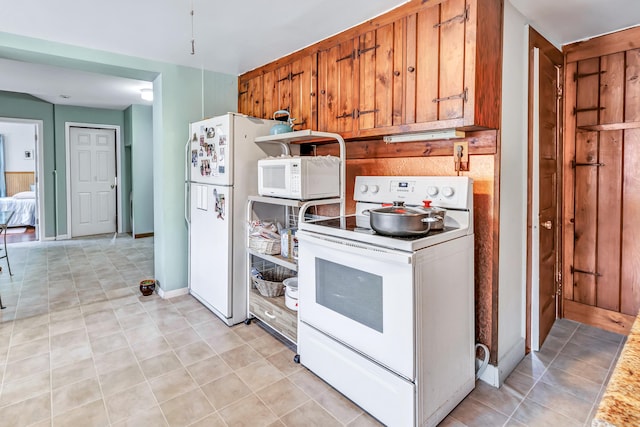 kitchen featuring white appliances, light tile patterned floors, brown cabinetry, and baseboards