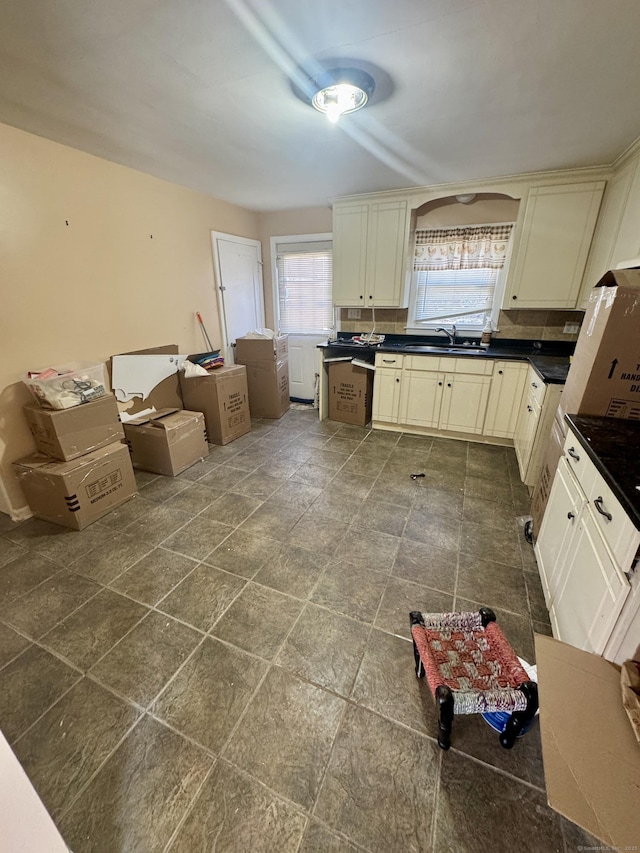 kitchen featuring dark countertops, cream cabinets, a healthy amount of sunlight, and backsplash