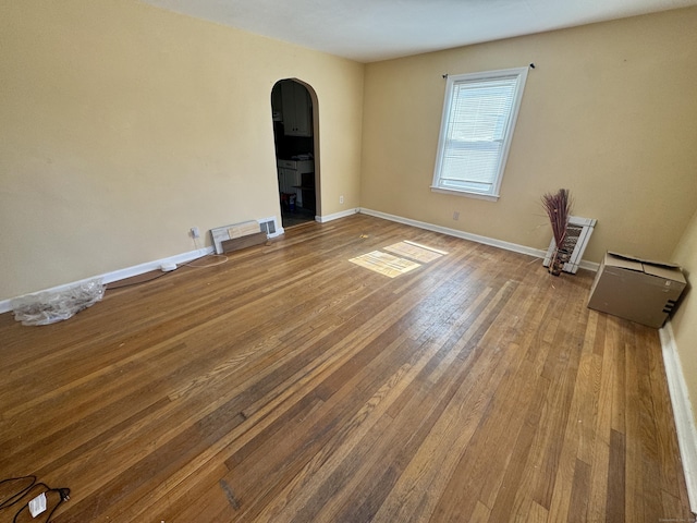 empty room with baseboards, arched walkways, visible vents, and hardwood / wood-style floors