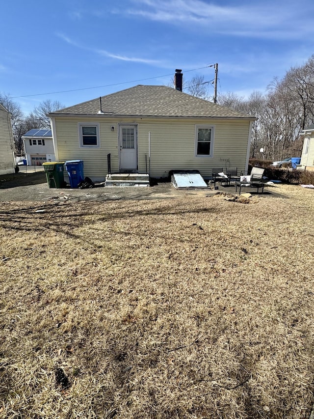 rear view of house featuring a chimney and roof with shingles