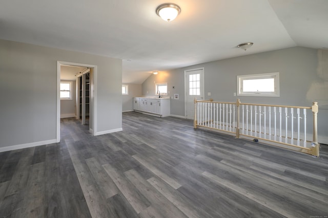 unfurnished room with dark wood-style floors, baseboards, lofted ceiling, and a sink