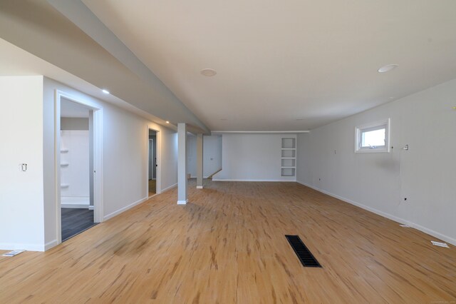 basement with light wood-type flooring, visible vents, baseboards, and built in shelves