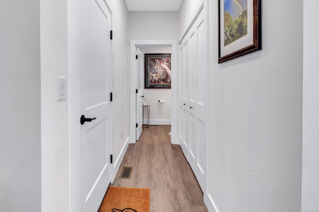 hall with visible vents, light wood-style flooring, and baseboards