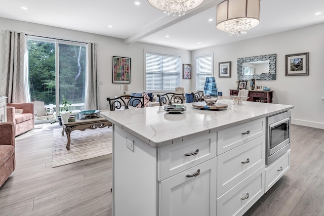 kitchen with light stone counters, stainless steel microwave, a kitchen island, white cabinets, and light wood finished floors