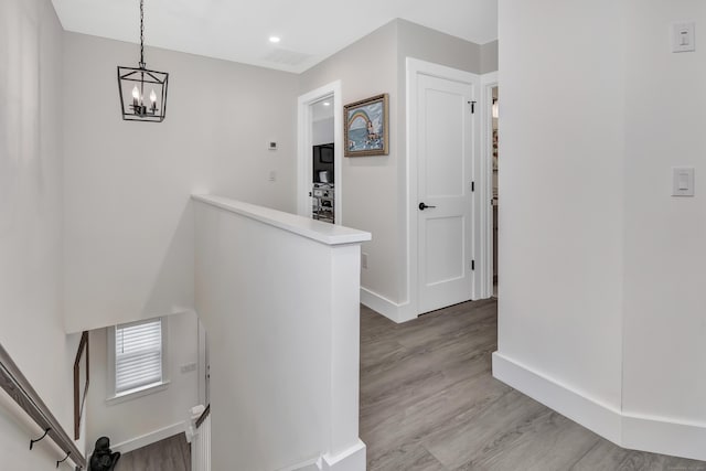 hallway featuring an upstairs landing, a notable chandelier, light wood-type flooring, and baseboards