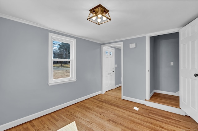 spare room featuring light wood-style flooring, an inviting chandelier, baseboards, and ornamental molding