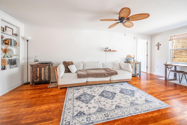 living area featuring built in features, baseboards, wood finished floors, and a ceiling fan