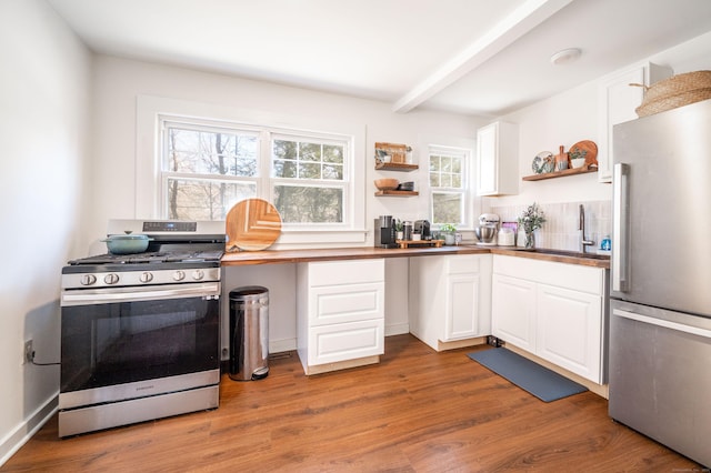 kitchen featuring wood finished floors, open shelves, a sink, stainless steel appliances, and built in desk