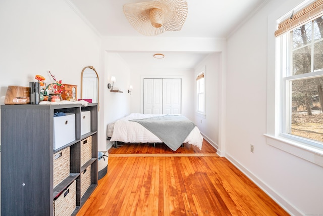 bedroom with a closet, light wood-style flooring, crown molding, and baseboards