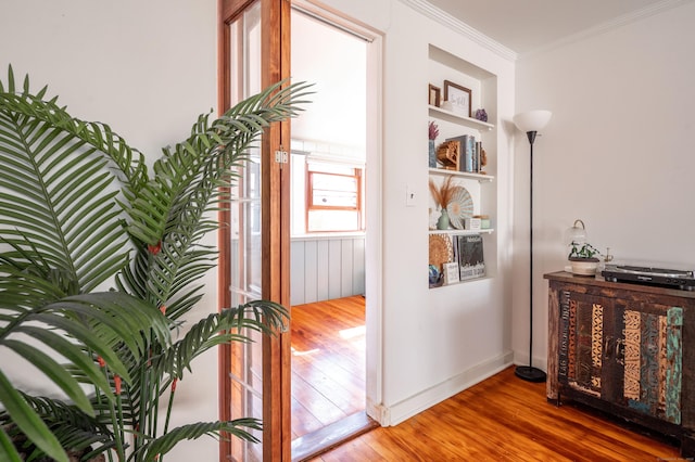 corridor featuring built in features, wood finished floors, baseboards, and ornamental molding