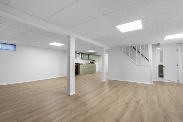 finished basement with light wood-style flooring, a paneled ceiling, and baseboards