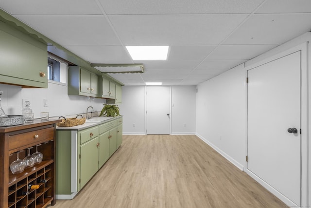 kitchen featuring light wood finished floors, baseboards, a drop ceiling, green cabinetry, and a sink