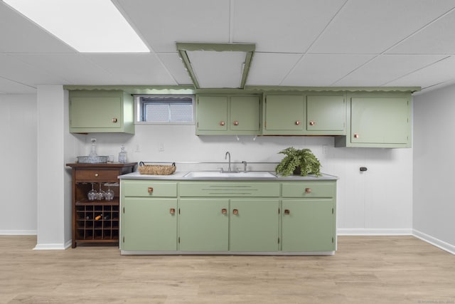 kitchen with light wood-style flooring, a sink, a drop ceiling, green cabinets, and baseboards