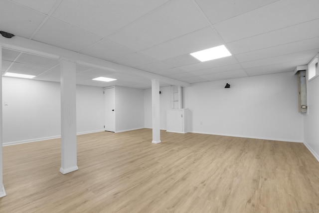 finished basement featuring a drop ceiling, light wood-style flooring, and baseboards