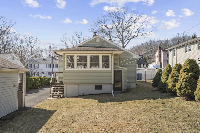 rear view of property with a lawn, roof with shingles, and fence