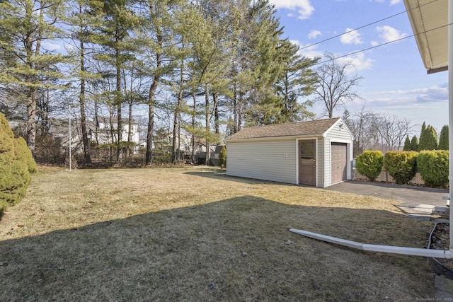 view of yard featuring an outbuilding, fence, a garage, and aphalt driveway