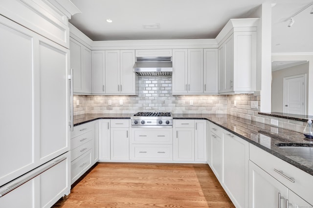 kitchen featuring light wood finished floors, dark stone counters, exhaust hood, stainless steel gas stovetop, and white cabinets