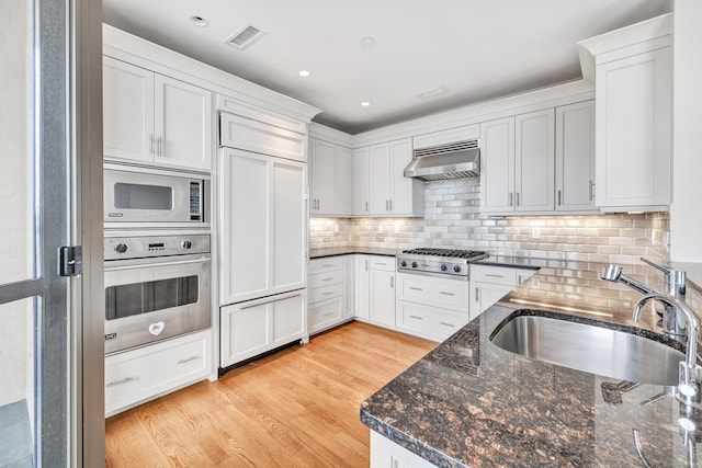 kitchen with visible vents, light wood-type flooring, a sink, exhaust hood, and built in appliances