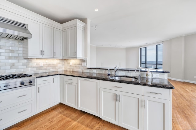 kitchen featuring stainless steel gas cooktop, dark stone counters, a sink, extractor fan, and tasteful backsplash