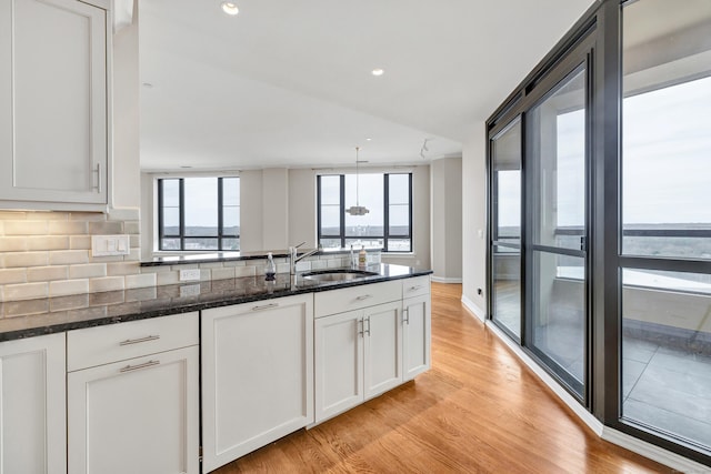 kitchen with a sink, dark stone counters, backsplash, and white cabinetry