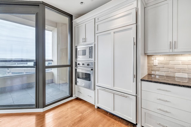 kitchen featuring tasteful backsplash, dark stone counters, light wood-style floors, white cabinets, and stainless steel appliances