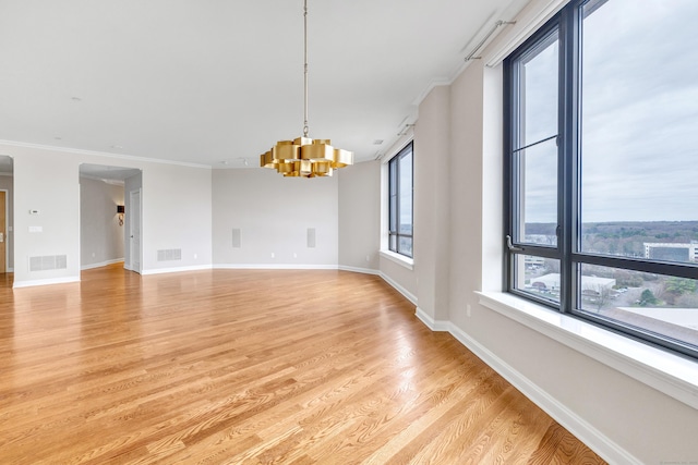 unfurnished room featuring baseboards, visible vents, light wood finished floors, crown molding, and a notable chandelier