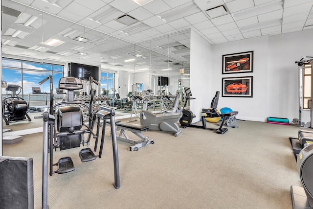 exercise room featuring carpet, a paneled ceiling, and baseboards