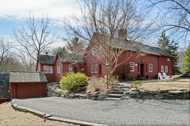 view of front facade featuring an attached garage, an outbuilding, gravel driveway, and a chimney