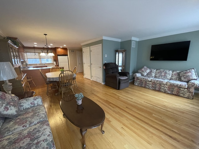 living area featuring a notable chandelier, recessed lighting, light wood-style flooring, and ornamental molding