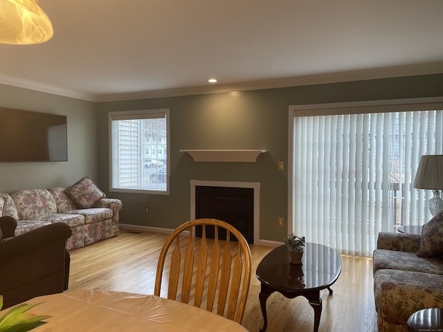 living room with light wood-style flooring, a fireplace, crown molding, and baseboards