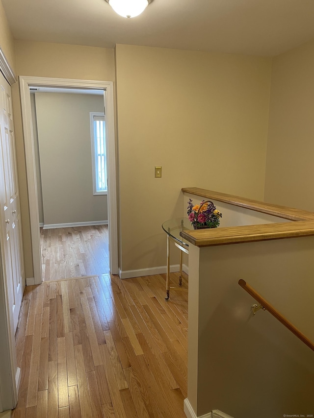 corridor featuring an upstairs landing, light wood-type flooring, and baseboards