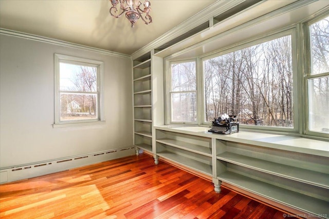 interior space with a healthy amount of sunlight, a baseboard heating unit, ornamental molding, an inviting chandelier, and wood finished floors