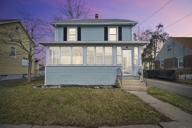 american foursquare style home with a front lawn, a sunroom, and a chimney