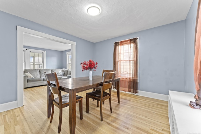 dining room with light wood-type flooring, baseboards, and a textured ceiling