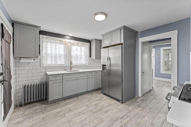 kitchen with radiator, a sink, gray cabinetry, light countertops, and stainless steel fridge