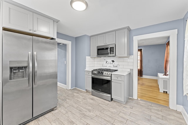 kitchen with gray cabinetry, stainless steel appliances, light wood finished floors, decorative backsplash, and light countertops