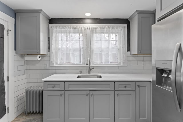kitchen featuring light countertops, radiator heating unit, gray cabinets, stainless steel fridge, and a sink