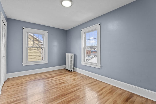 empty room featuring radiator heating unit, a healthy amount of sunlight, light wood-style floors, and baseboards