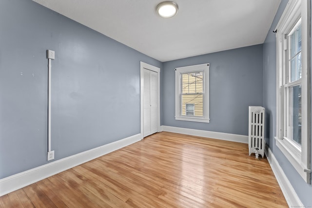 empty room with baseboards, radiator, and light wood-style flooring