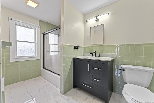 bathroom featuring tile walls, toilet, marble finish floor, and enclosed tub / shower combo