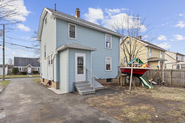 rear view of property with a playground, fence, entry steps, roof with shingles, and a chimney