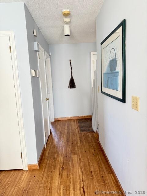 hall with light wood-style flooring, baseboards, and a textured ceiling