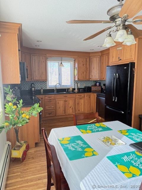 kitchen with a ceiling fan, a baseboard radiator, freestanding refrigerator, stainless steel microwave, and brown cabinets