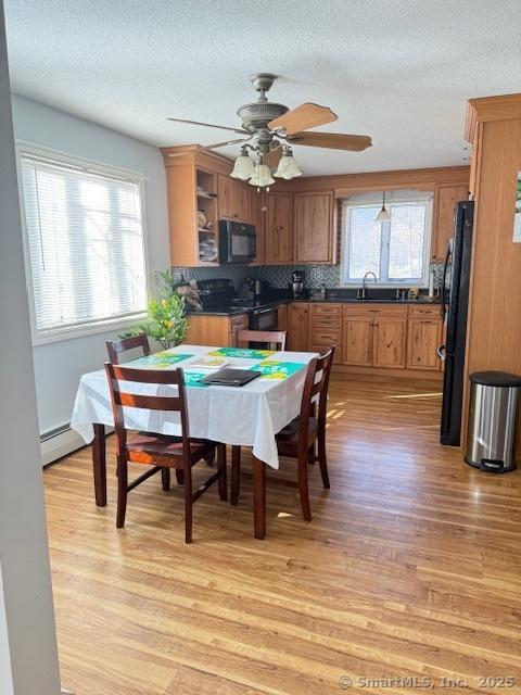 dining area with ceiling fan, light wood-type flooring, a wealth of natural light, and a baseboard radiator