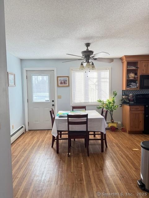 dining room with ceiling fan, baseboard heating, wood finished floors, and a textured ceiling