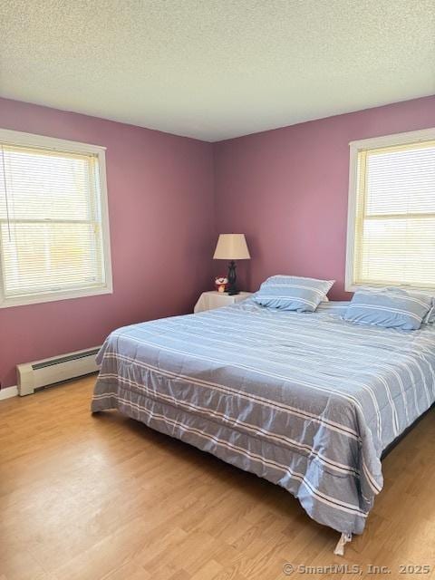 bedroom with multiple windows, light wood-style floors, and baseboard heating