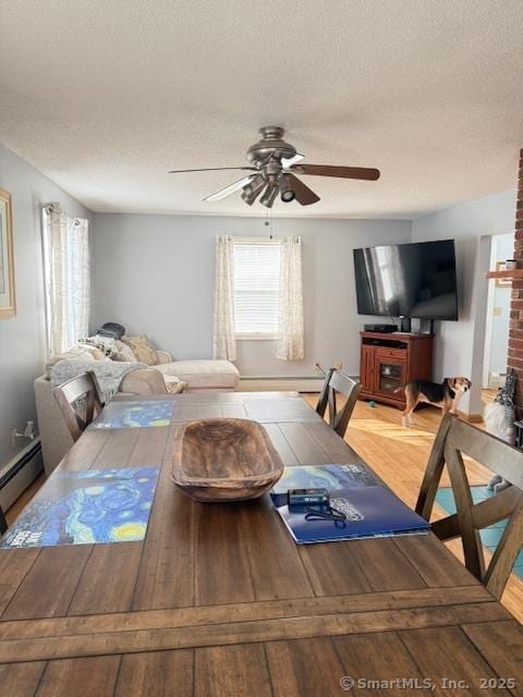 dining area with baseboard heating, a textured ceiling, light wood-style floors, and a ceiling fan