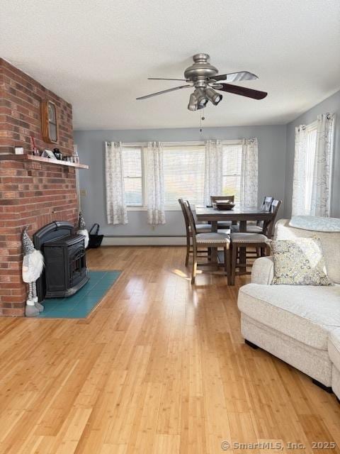 living room with light wood-type flooring, plenty of natural light, ceiling fan, and a wood stove