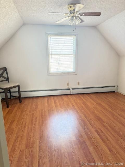 additional living space featuring a textured ceiling, lofted ceiling, light wood-style floors, and a ceiling fan